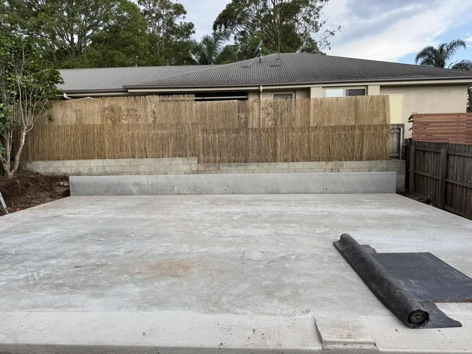 Concrete area with a raised edge beside boundary fencing.